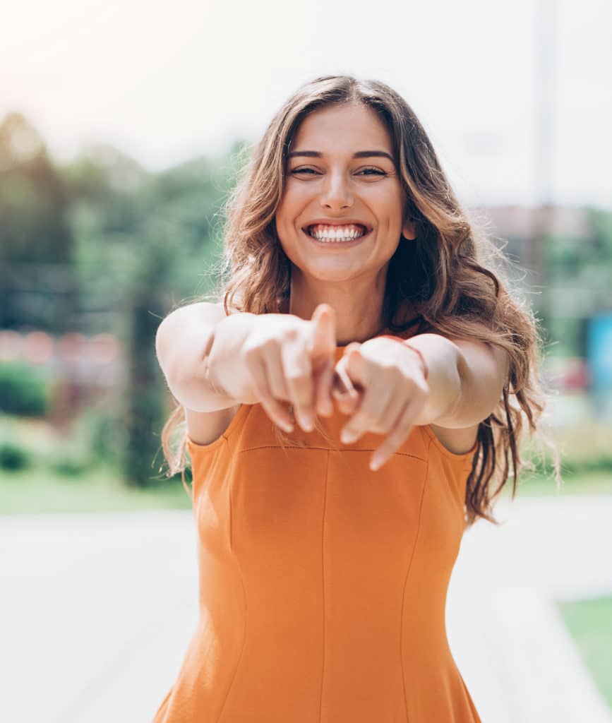 woman pointing both hands at camera playfully while smiling widely outside in the sun