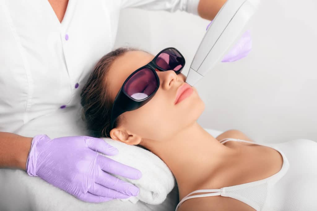 close up of woman laying down with sunglasses on as man adjusts towel under her head