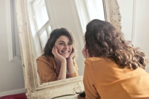 woman staring in mirror with hands on her face smiling widely