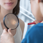Oncologist examining female patient with magnifier in clinic