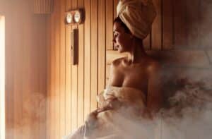 woman relaxing and sweating in hot sauna wrapped in towel