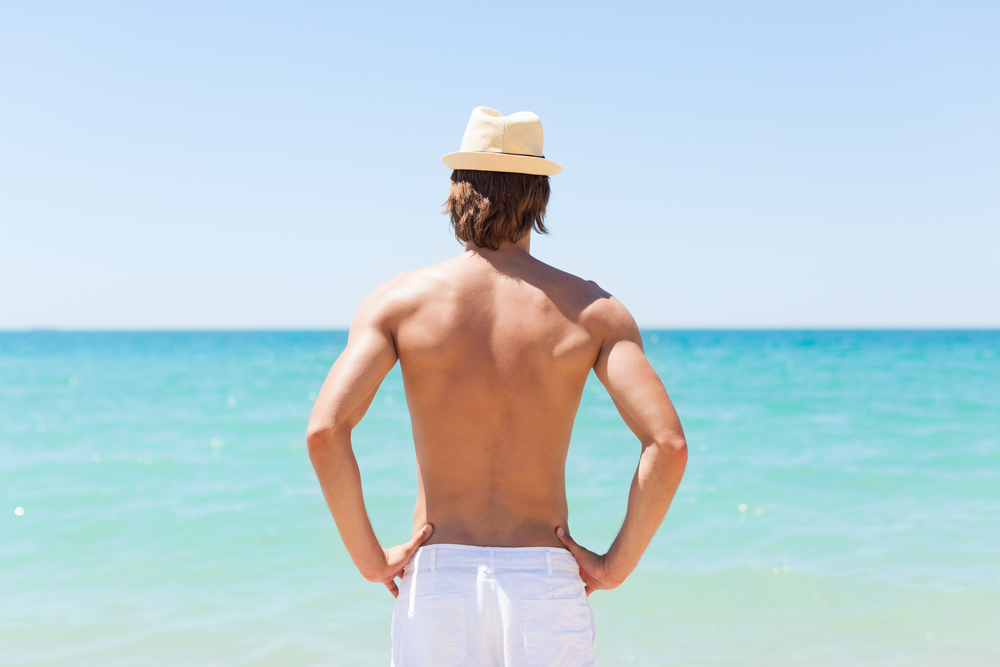 Man at the beach with no top, showing his hair-free back from back laser hair removal in NYC
